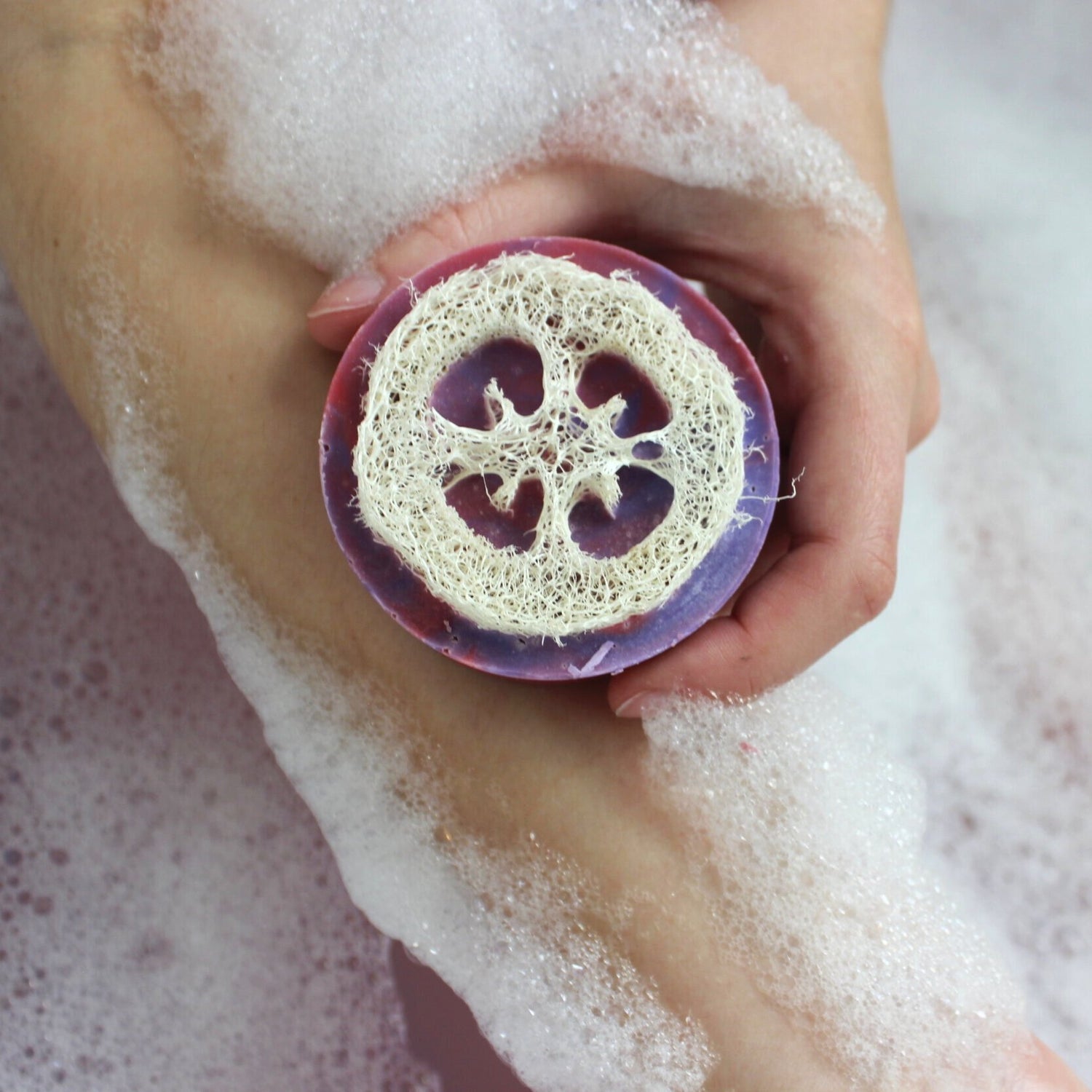 A person holding a bar of soap in a bubbling bath, with the soap partially covered