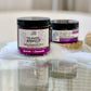 Two jars of 'The Sensitive Exorcist Lavender Chamomile Scrub'  on a reflective surface.