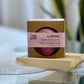 A shampoo bar packaged in a cardboard box with a clear window, placed on a wooden surface, with a blurred background.