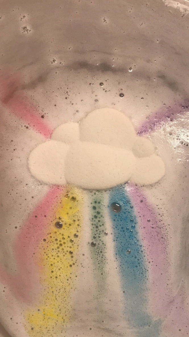 Cloud-shaped bath bomb with colorful rainbow trail in a bathtub