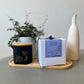 A Butter Massage Candle is displayed on a wooden tray alongside a plant and a vase, with the candle's packaging showing 'Signature Spa' and a butterfly graphic.