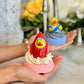 Two rocket-shaped bath bombs with blue and pink fizz, being held in a person's hands with a decorative background.