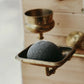 A bamboo charcoal-enriched konjac sponge resting in a metal holder with a gold-colored finish.