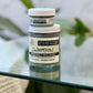 A jar of Swampthing Activated Charcoal Mud Mask with its lid on, placed on a glass surface with a plant in the background.