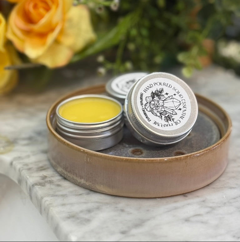 solid perfume tins displayed with one open to show a light yellow color and smooth balm. 