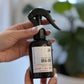 A hand holding a black spray bottle labeled 'Bug Off!' with a plant in the background
