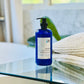 A blue bottle of liquid conditioner with a pump, placed on a glass surface with a blurred background.