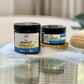 Two jars of The Exorcist Lemon Mint Scrub, one larger and one smaller, placed on a surface with bubbles sprinkled around. The larger jar is in the foreground, and the smaller one is in the background.