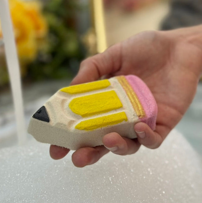 Hand holding a pencil-shaped bath bomb under running water.
