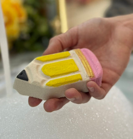 Hand holding a pencil-shaped bath bomb under running water.