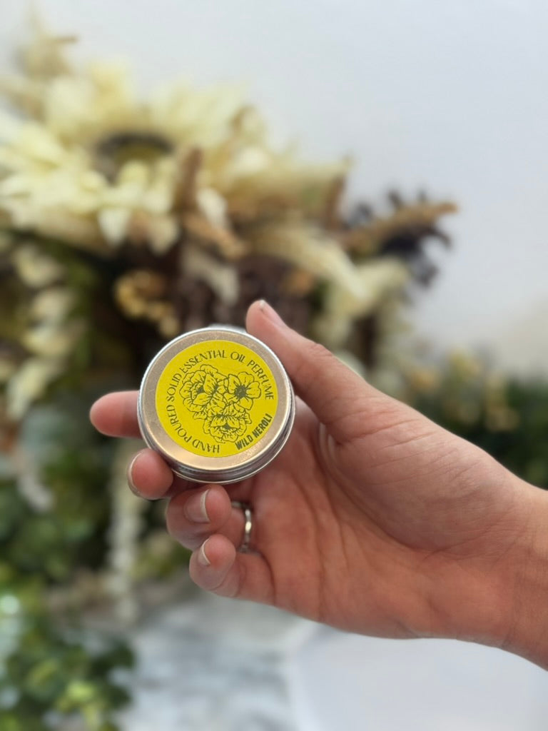 Hand holding a small round container with a yellow label against a blurred natural background