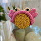 A pink headband designed to look like a crab with a large sea sponge attached to it, placed on a reflective surface.
