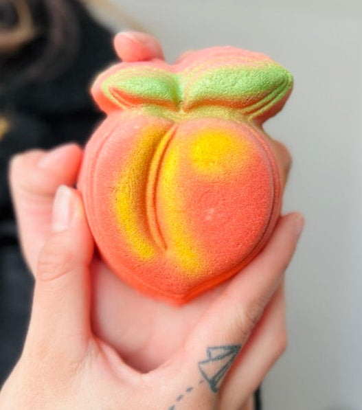 Peach-shaped bath bomb held in a hand with a blurred background