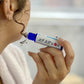 A person is holding a blue and white essential oil roller to their face, specifically on an acne-covered cheek.