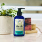 A pump bottle of Aloe-ah Body Lotion with a label showing the product name and a green aloe leaf, placed on a countertop with a potted plant and other items in the background.