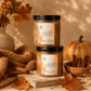 Two jars of Jelly Sculp skincare body butter in vanilla + cinnamon scent, stacked on a stone slab with autumn props including a knit blanket, dried leaves, cinnamon sticks, a small pumpkin, and a vase in a warm, cozy setting.