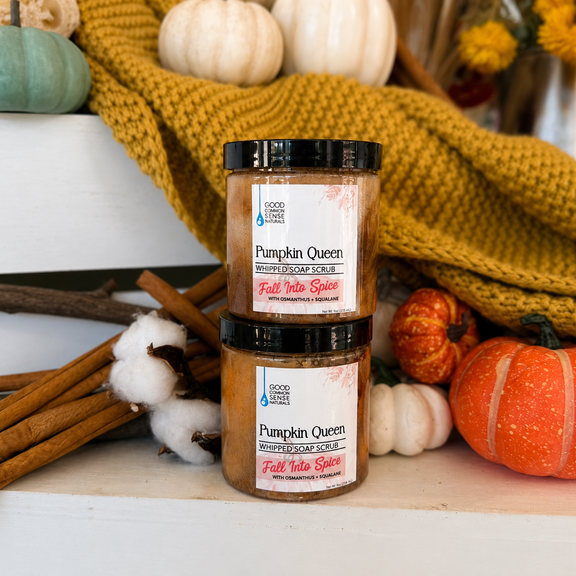 Two jars of Good For You Soap Co. Pumpkin Queen Fall Vibes soap scrub stacked on a white surface, surrounded by autumn props including pumpkins, a yellow knit blanket, cinnamon sticks, and cotton bolls.