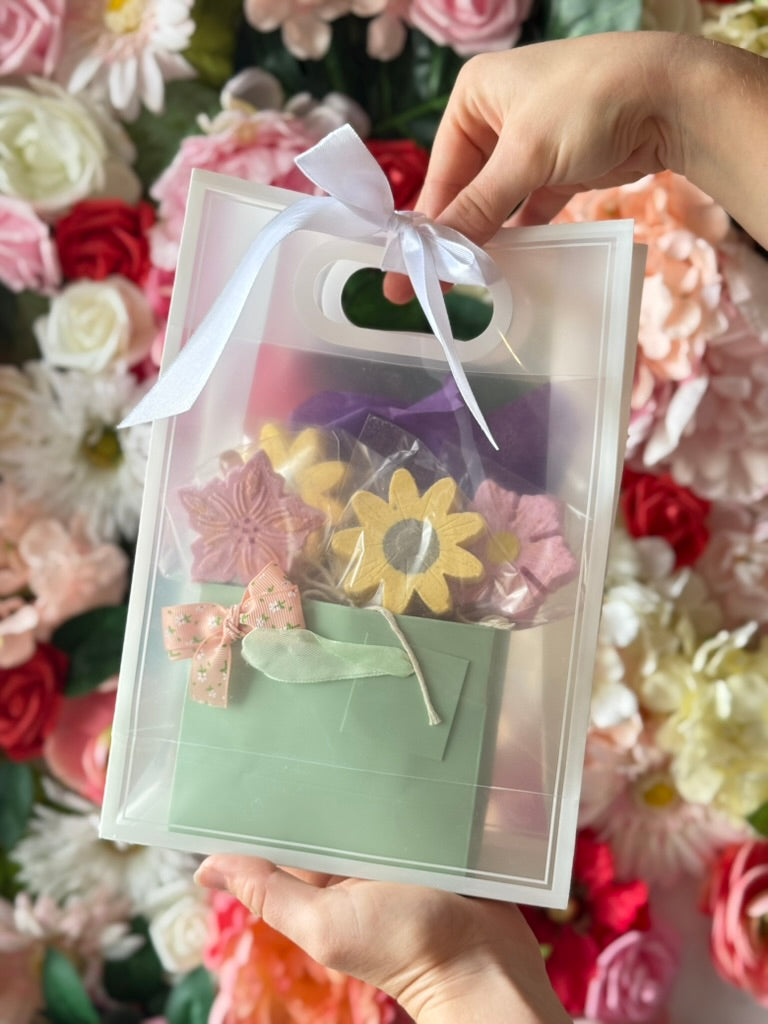 Clear gift bag with 5 flower bath bombs held in front of a floral background