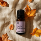 A 10 ml bottle of Coco Brand Pure Essential Oils placed on a textured beige linen fabric, surrounded by scattered orange and yellow autumn leaves under warm, directional sunlight.