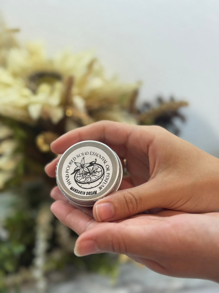 Hand holding a small metal container with a decorative label against a blurred natural background