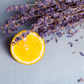 A photo of a slice of lemon next to a bundle of dried lavender, with a blurred background.