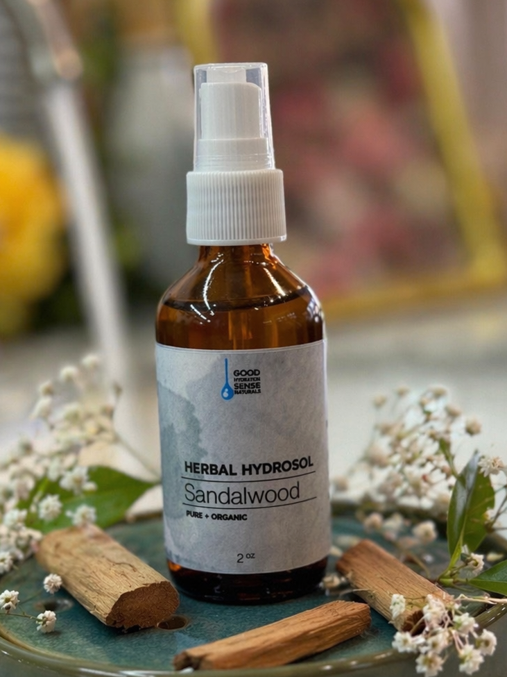 Sandalwood hydrosol bottle on a decorative tray with sandalwood sticks and flowers.