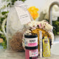 A gift set for spa night including a spa headband, large vegan sea sponge, pink sugar scrub,  hand cream, and lip balm with a cozy holder, all displayed on a marble surface.