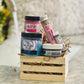 A variety of bath and body products packaged in a wooden gift box, including a jar labeled 'BEET IT', a lip scrub, a lip balm, a bath salt tube labeled 'HERBIVORE', and a jar of 'BUFF MY SOUL'.