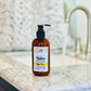 A bottle of Native Body Lotion - High Pine rests on a marble countertop near a sink, with a blurred white textured background, offering smooth skin enriched with essential oils.