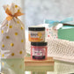 A gift set containing two jars of skin care products, one labeled 'Handy' and the other 'Buff My Soul', with a polka-dot themed gift bag and a decorative cloth in the background.