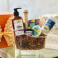A spa gift set containing various bath and body products, neatly arranged in a clear container with a keepsake bathtub for packaging. The set is adorned with decorative flowers and a bow, presented alongside a colorful gift box.