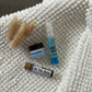 A set of three travel-sized cosmetic products including a lip balm, hand sanitizer, and a spa cream, displayed on a textured white surface.