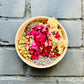 Anxiety Relief Ritual Bath herbs in a brown bowl filled with Herbal Bath Ingredients: lavender, chamomile, holy basil, skullcap, chrysanthemum, rose. with black bricked backround 