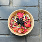 A bowl filled with anti-inflammatory herbal bath ingredients such as chamomile, lavender, white sage, yarrow, elderberry, clove, and rose, placed on a dark surface.
