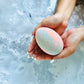 A person holding a bath bomb shaped like an Easter egg with a marbled pink and blue color pattern.