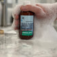 A bottle of Sasquwash Beard Poo with bubbles, set against a backdrop of a kitchen with soap bubbles around.