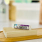 A tube of Tortoise Lavender Lip Balm placed on a wooden surface with a blurred kitchen background.
