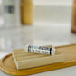 A tube of 'In The Nude, Lip Balm' resting on a wooden tray with a blurred background.