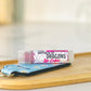 A tube of pink lipstick labeled mother of Dragons with a blue and white patterned case, resting on a bamboo makeup tray. 