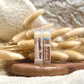 Two sticks of 'Vanilla Kiss' lip balm next to a decorative dry plant, on a textured background.
