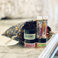 Three containers of hand cream and lip balm placed inside a fabric bag with a floral pattern. The containers are labeled with various names such as 'Handy', 'Joyful', and 'Tortoise'.