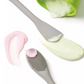 A silicone scrub brush and spatula tool with a grey handle, with a pink and light green facial mask being applied to it.