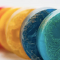 A set of six loofah soaps in various colors including blue, green, yellow, orange, pink, and gray, each with a different color and texture.