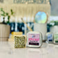 A massage lotion bar with a citrus scent, displayed in a clear container on a bright surface, with decorative plants and a mirror in the background.