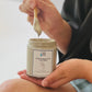 women holding a jar filled with the mediterranean mud body mask scooping with a wooden spoon. 