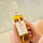 A person holding a bottle of custom body oil with a yellow hue and a white spray nozzle. 
