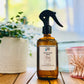 A clear spray bottle with a black spray nozzle, labeled, room and linen spray 