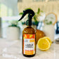 A black spray bottle labeled 'Lounge Joyful, Room & Linen Spray' with orange and bergamot design, placed on a marble surface with a lemon beside it.