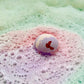 purple pink and green bath bomb in water bubbling 