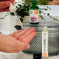 A close-up image of a hand holding a bottle of Vibrance Deep Hydration Face Serum, with a dropper, in front of a larger container placed on a marble surface. The background includes a plant and a blurred object.
